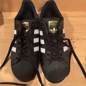 Adidas Superstar Black Sneakers with White Stripes and Gold Logo.
